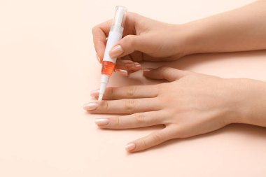 Bej arka planda kalemle tırnak eti yağı süren kadın eller