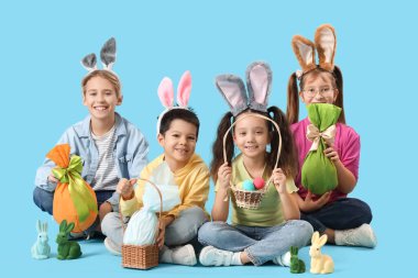 Mavi arka planda oturan tavşan kulaklı küçük çocuklar.