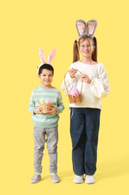 Sarı arka planda Paskalya yumurtaları olan tavşan kulaklı küçük çocuklar.