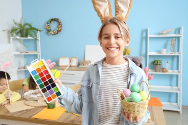 Tavşan kulaklı küçük çocuk Paskalya yumurtaları ve odada boyaları var.