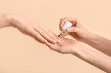 Bej arka planda tırnak eti yağı uygulayan kadın eller