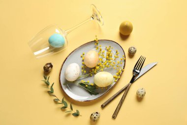 Sarı arka planda Paskalya yumurtaları ve mimoza çiçekleri olan güzel bir masa.