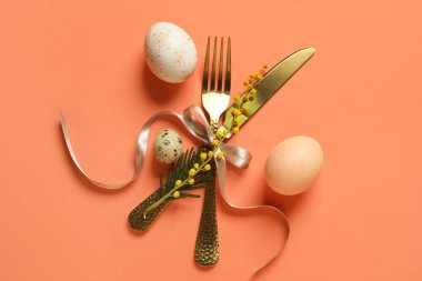 Turuncu arka planda Paskalya yumurtası ve mimoza çiçekli sofra takımı.