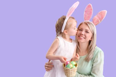 Paskalya yumurtası taşıyan küçük bir kız annesini leylak arka planda öpüyor.