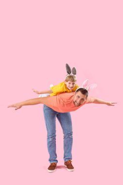 Babası tavşan kulaklı küçük çocuk pembe arka planda eğleniyor. Paskalya kutlaması