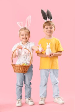 Pembe arka planda Paskalya yumurtaları olan tavşan kulaklı çocuklar.