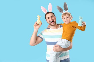 Babası tavşan kulaklı küçük bir çocuk ve mavi arka planda Paskalya tavşanları.