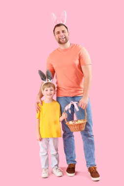 Pembe arka planda Paskalya yumurtaları olan tavşan kulaklı küçük çocuk ve babası