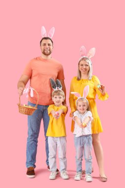 Pembe arka planda Paskalya yumurtaları olan tavşan kulaklı mutlu bir aile.