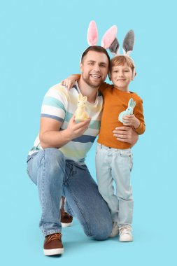 Babası tavşan kulaklı küçük bir çocuk ve mavi arka planda Paskalya tavşanları.