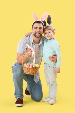Mutlu baba ve küçük oğlu, sarı arka planda sarılan Paskalya yumurtalarıyla tavşan kulaklı.
