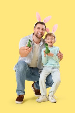 Mutlu baba ve küçük oğlu tavşan kulaklı, sarı arka planda Paskalya tavşanları