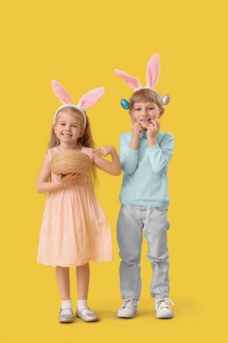 Sarı arka planda Paskalya yumurtaları olan tavşan kulaklı küçük çocuklar.