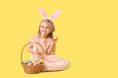 Tavşan kulaklı küçük kız Paskalya yumurtaları sarı arka planda oturuyor.