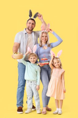 Sarı arka planda Paskalya yumurtaları olan tavşan kulaklı mutlu bir aile.