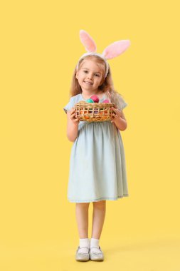 Sarı arka planda Paskalya yumurtaları olan tavşan kulaklı küçük kız.