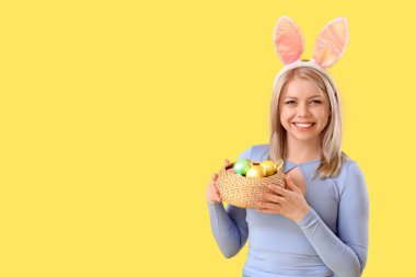 Sarı arka planda Paskalya yumurtaları olan tavşan kulaklı güzel bir kadın.