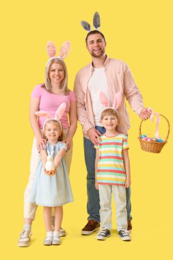 Sarı arka planda Paskalya yumurtaları olan tavşan kulaklı mutlu bir aile.