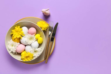 Paskalya yumurtaları ve eflatun arkaplanda kasımpatı çiçekleri olan güzel bir masa.