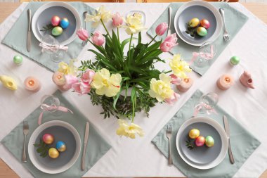 Çiçekler, çatal bıçak takımı, mumlar ve boyalı yumurtalarla süslü Paskalya sofrası.