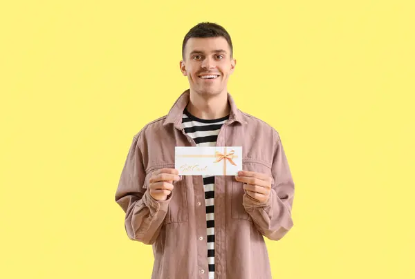 黄色の背景にギフトカードを持つ若い男 — ストック写真