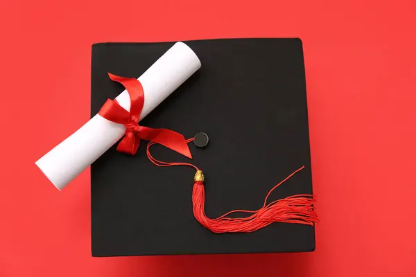 stock image Graduation hat and diploma on red background