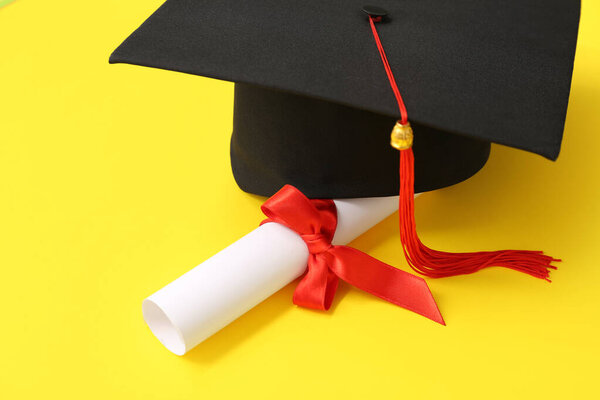 Graduation hat and diploma on yellow background
