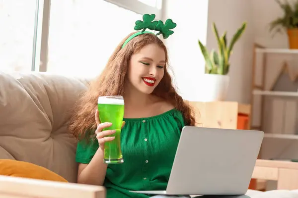 Young woman with beer using laptop at home on St. Patrick\'s Day