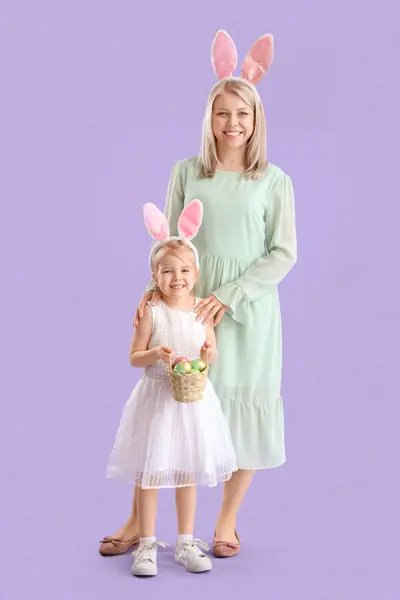 有复活节彩蛋的小女孩和她有紫丁香背景的妈妈 — 图库照片