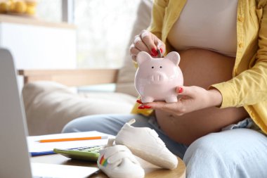 Genç hamile kadın evdeki domuz kumbarasına para koyuyor, yakın plan. Annelik Faydası kavramı