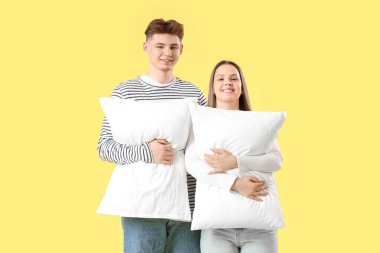 Sarı arka planda yastıkları olan genç çift.