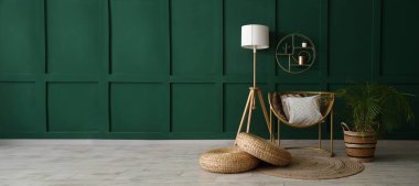 Yastıklı şık bir koltuk, hasır puflar, yer lambası ve yeşil duvarın yanındaki bitki örtüsü. Tasarım için pankart