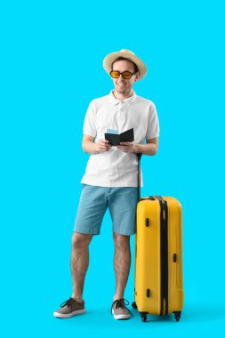 Mavi arka planda pasaportu ve bavulu olan erkek turist.