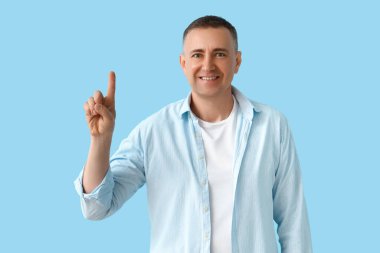 Olgun adam mavi arka plandaki bir şeyi işaret ediyor.