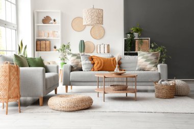 Interior of light living room with grey sofas, coffee table and wicker poufs clipart