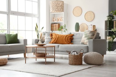 Gri koltukları, sehpası ve hasır pufları olan aydınlık oturma odasının içi.