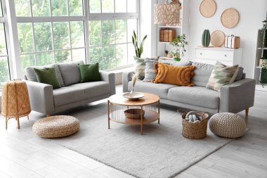 Gri koltukları, sehpası ve hasır pufları olan aydınlık oturma odasının içi.