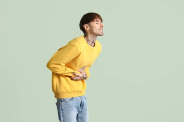 Yeşil arka planda karın ağrısı çeken genç bir adam.