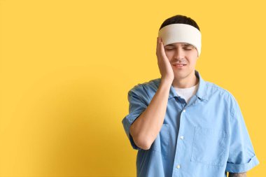 Beyin sarsıntısı geçiren ve sarı arka planda bandajlı genç bir adam.