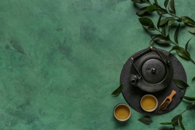 Fincanlı çaydanlık, bir kepçe kuru çay ve yeşil grunge arka planda yapraklar