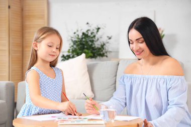 Küçük kızı evde resim çizerken mutlu bir anne.