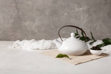 Çaydanlıklı bambu hasırı ve arka planda bir kase kuru çay.