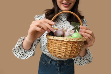 Paskalya sepeti tutan genç bir kadın. Arka planda kozmetik ürünler var. Yakın plan.