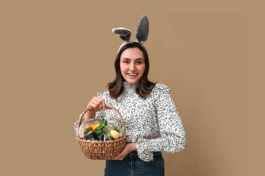 Tavşan kulaklı genç bir kadın elinde dekoratif kozmetik ürünlerle Paskalya sepeti tutuyor.