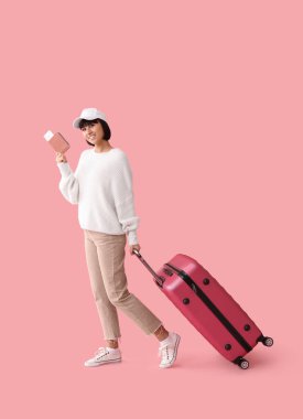 Pasaportu ve bavulu pembe arka planda olan bir kadın turist.