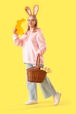 Paskalya sepeti, tavşan kulağı ve sarı arka planda dekor olan genç bir kız.