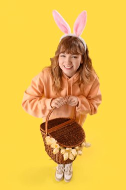 Sarı arka planda Paskalya tavşanı kulakları ve sepeti olan genç bir kız.