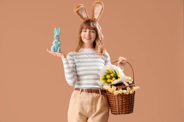 Paskalya tavşanı kulaklı, sepetli ve bej arka planda oyuncak tavşanlı genç bir kız.