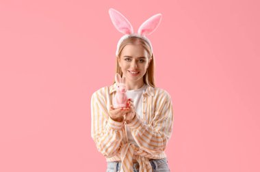 Paskalya tavşanı kulakları ve pembe arka planda oyuncak tavşanı olan genç kız.