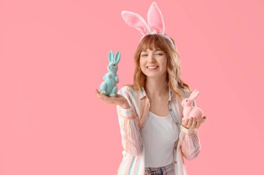 Paskalya tavşanı kulakları ve pembe arka planda oyuncak tavşanları olan genç bir kız.